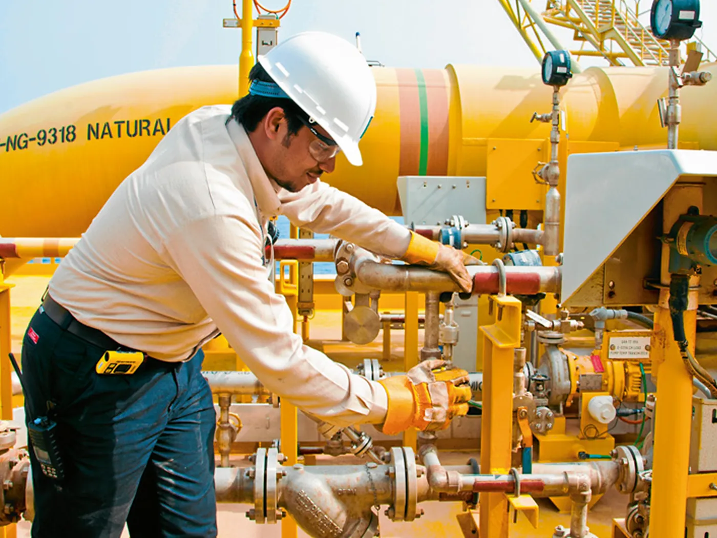 Technician in a hard hat and safety glasses adjusting valves on natural gas pipework